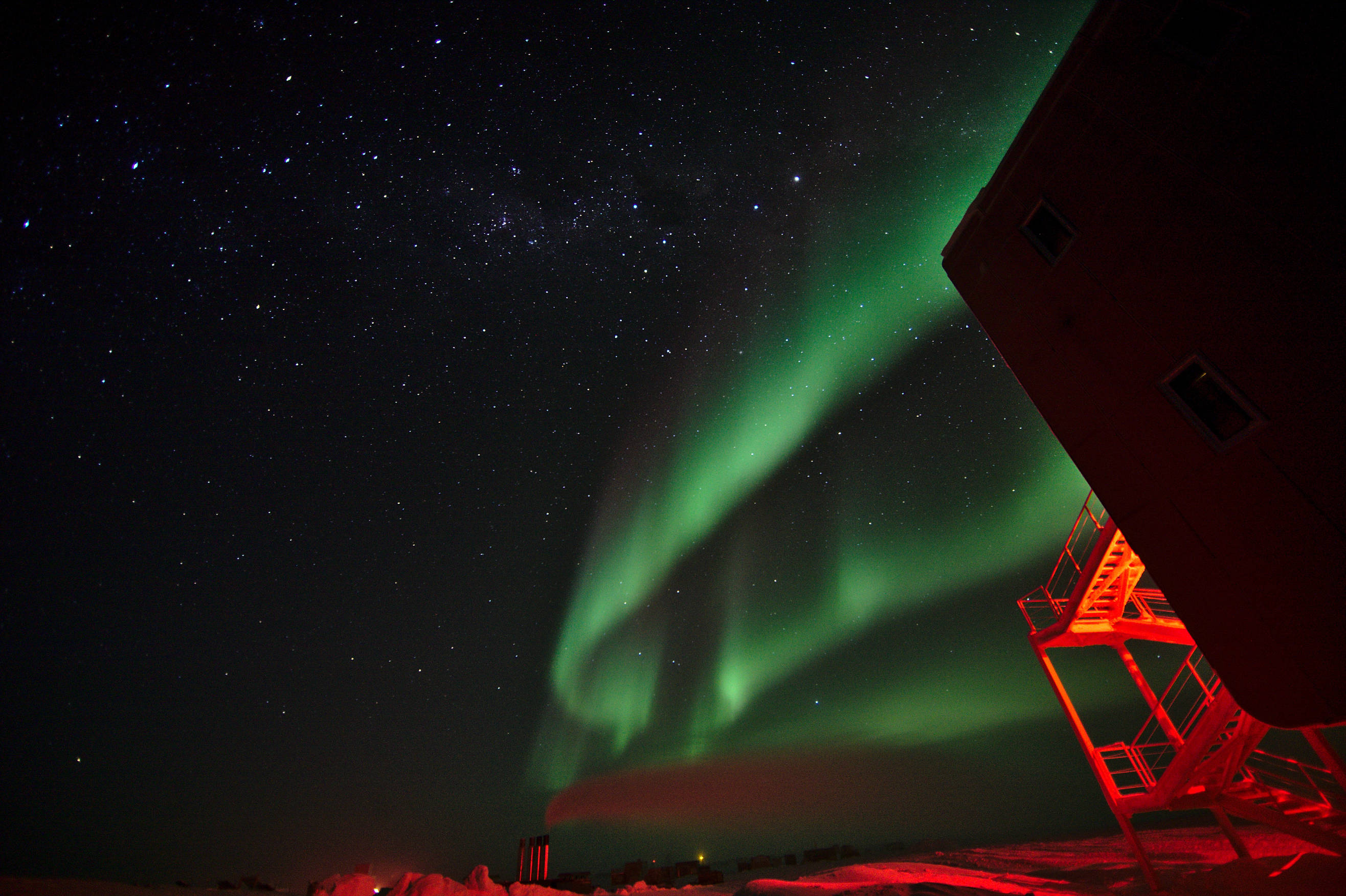 Auroras above the summer camp and power plant. To the right a corner of the station building with the red-illuminated emergency exits