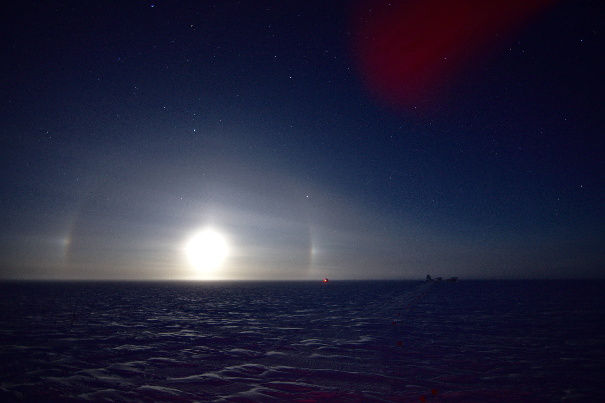 Ice crystals in the atmosphere cause the moonlight to form a partial halo and moon dogs around the full moon.