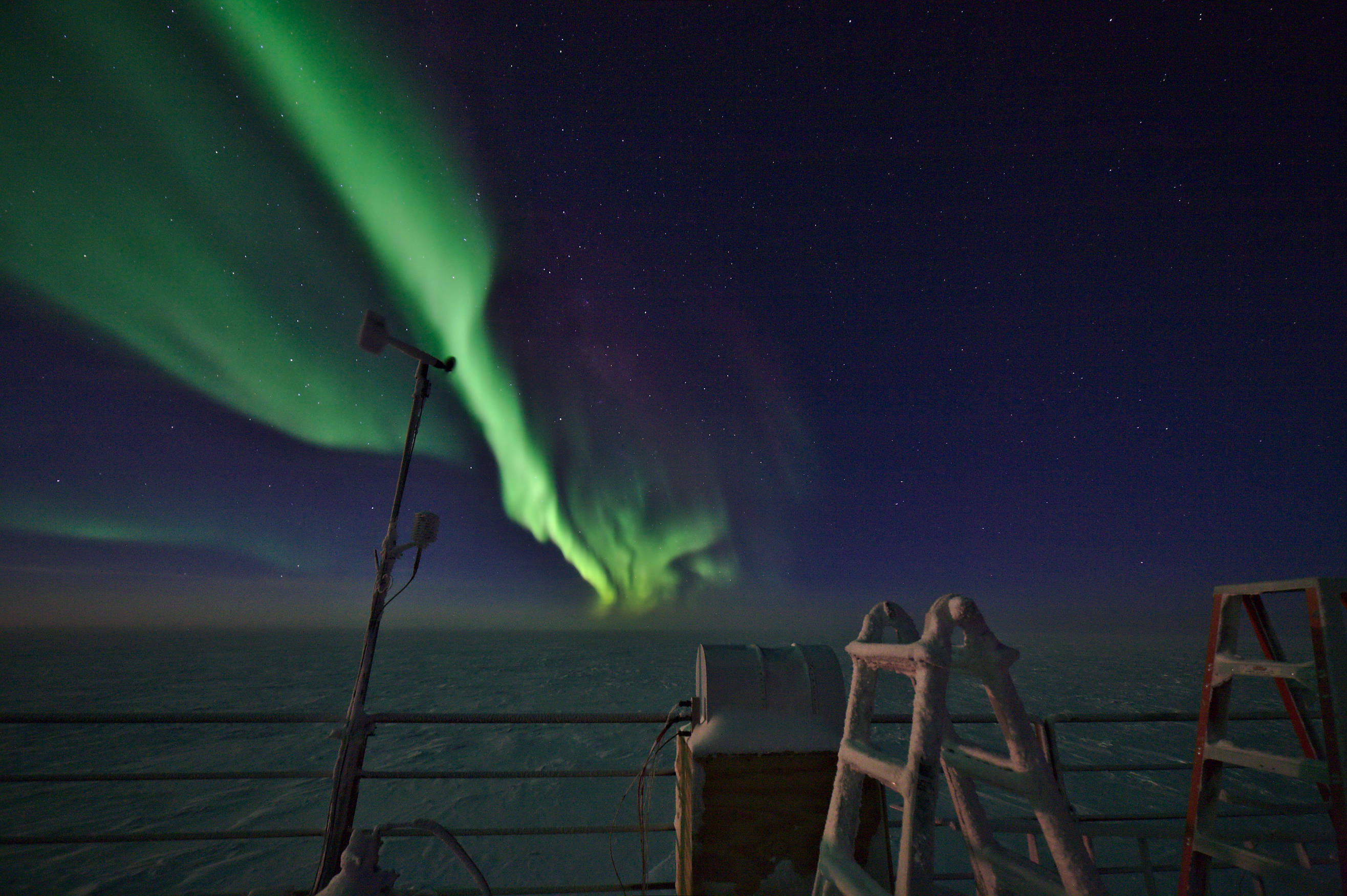 Strong auroras above the roof of the dark sector laboratory.  The light of the moon coming from the left illuminates the snow-covered ladder and the instruments of our weather station.