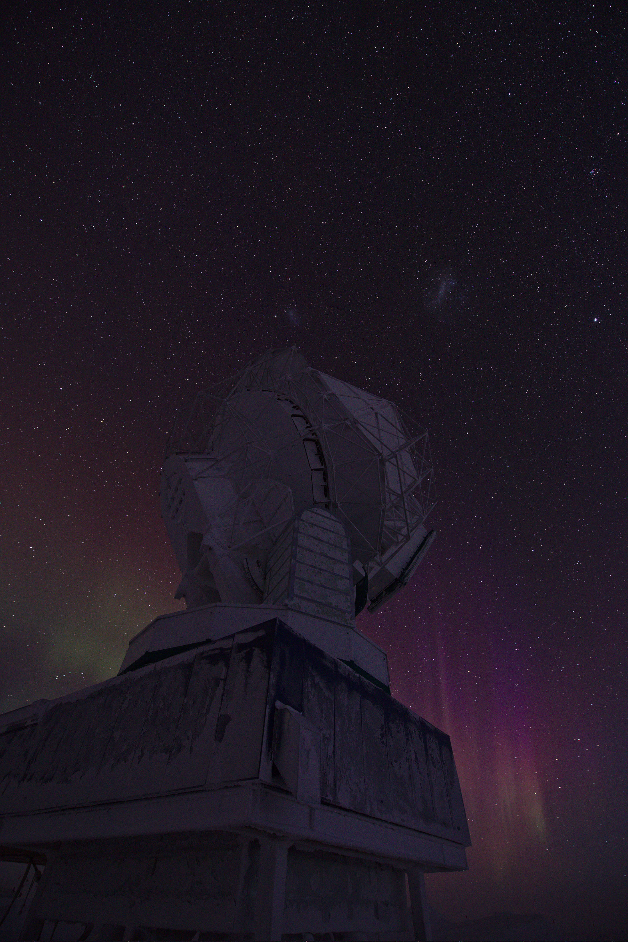 South Pole Telescope from below, with auroras on the horizon and the Magellanic Clouds above the telescope